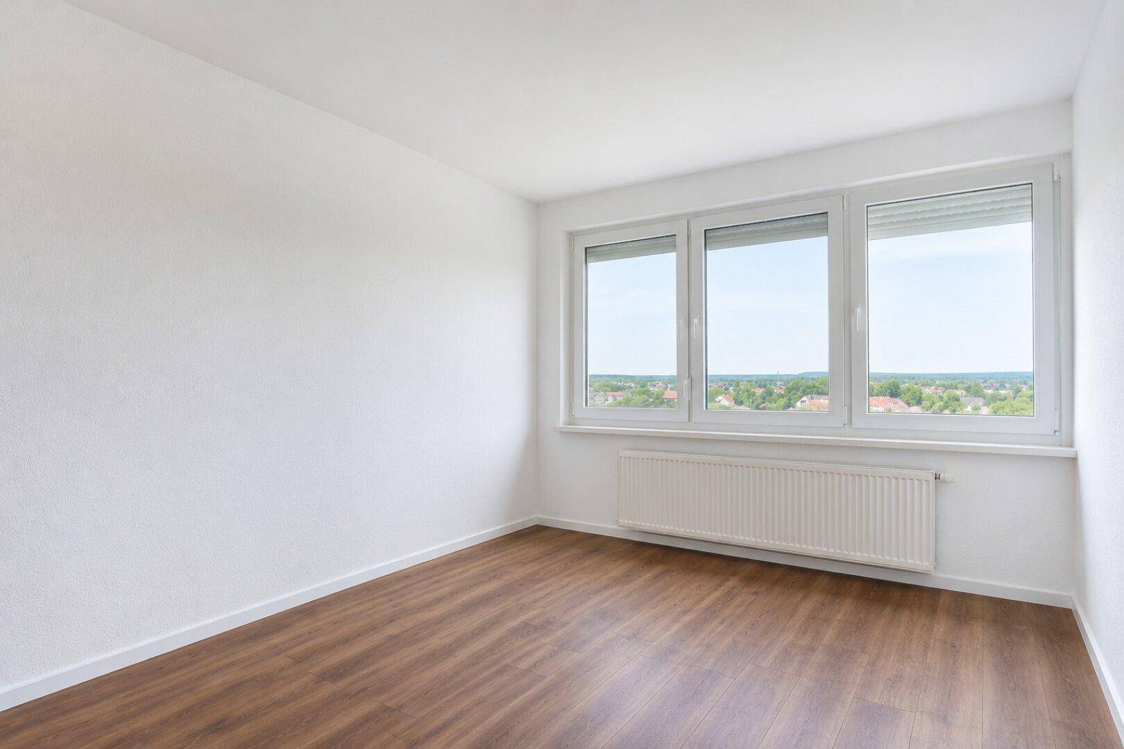 Leeres Schlafzimmer mit Laminatboden und weitem Blick aus dem Fenster.