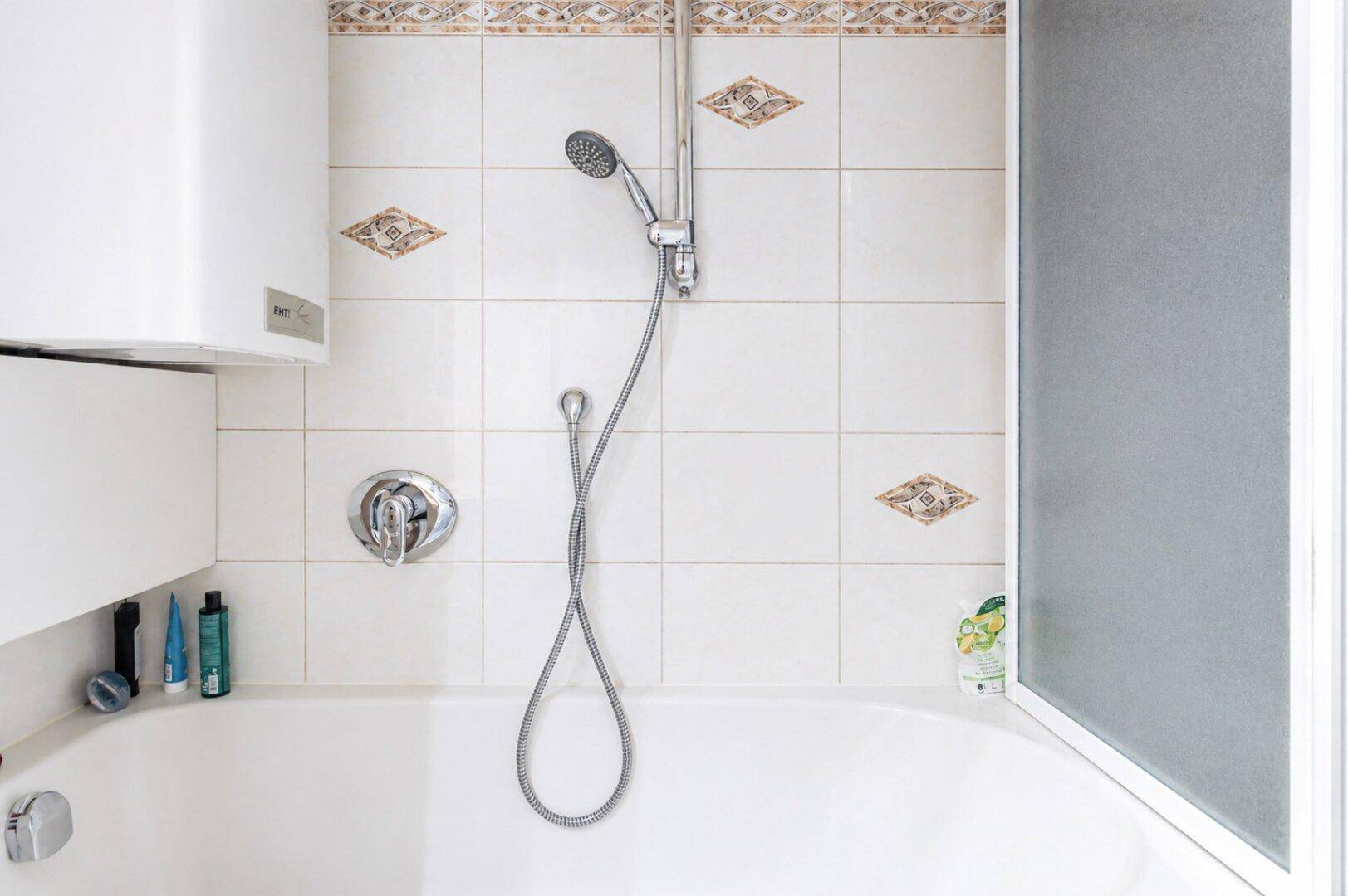 Badezimmer mit Badewanne und Duschkopf, umgeben von hellen Fliesen.