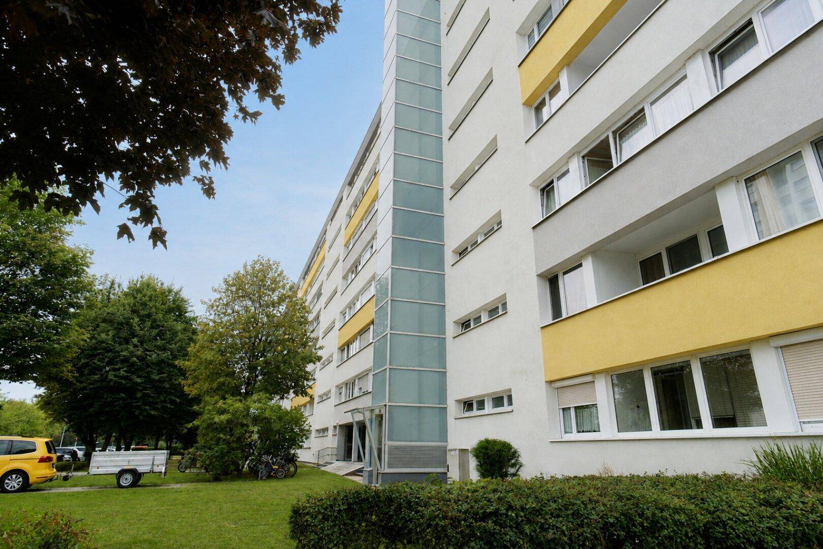 Fassade eines Mehrfamilienhauses mit Balkonen und externem Aufzug.