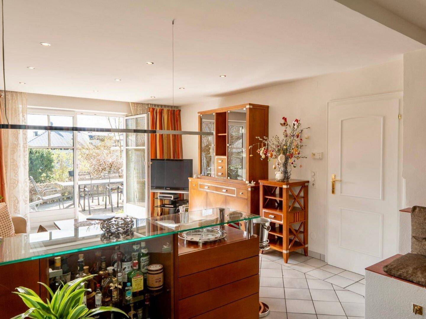 Helles Wohnzimmer mit Bar, Fliesenboden und Zugang zu einer sonnigen Außenterrasse.