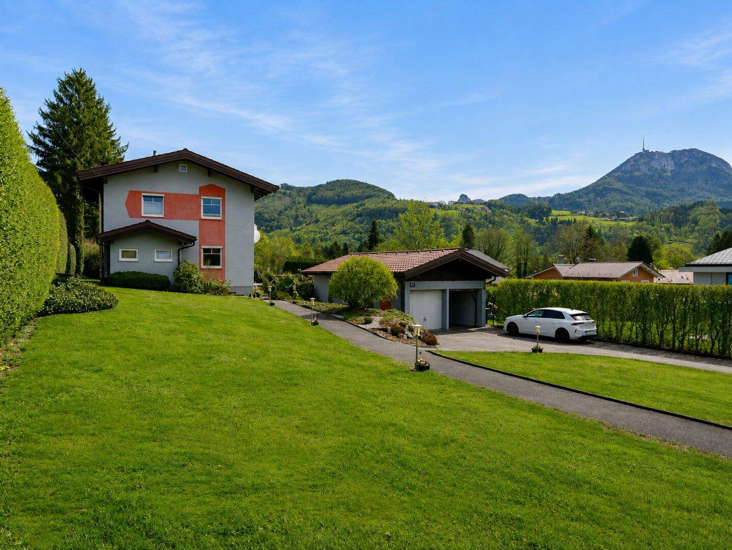 Einfamilienhaus mit großem gepflegten Rasen, Auffahrt und Blick auf die grüne Berglandschaft.