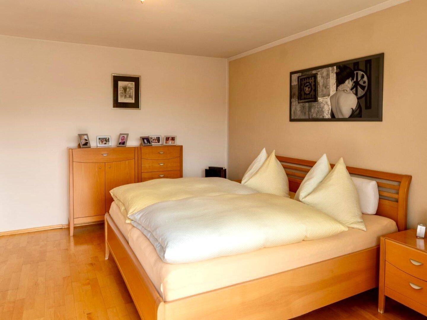 Gemütliches Schlafzimmer mit hellem Holzbett, Kommode und Parkettboden.