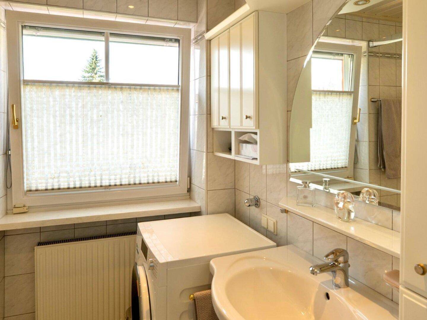 Funktionales Badezimmer mit Waschbecken, Waschmaschine und Fenster für Tageslicht.