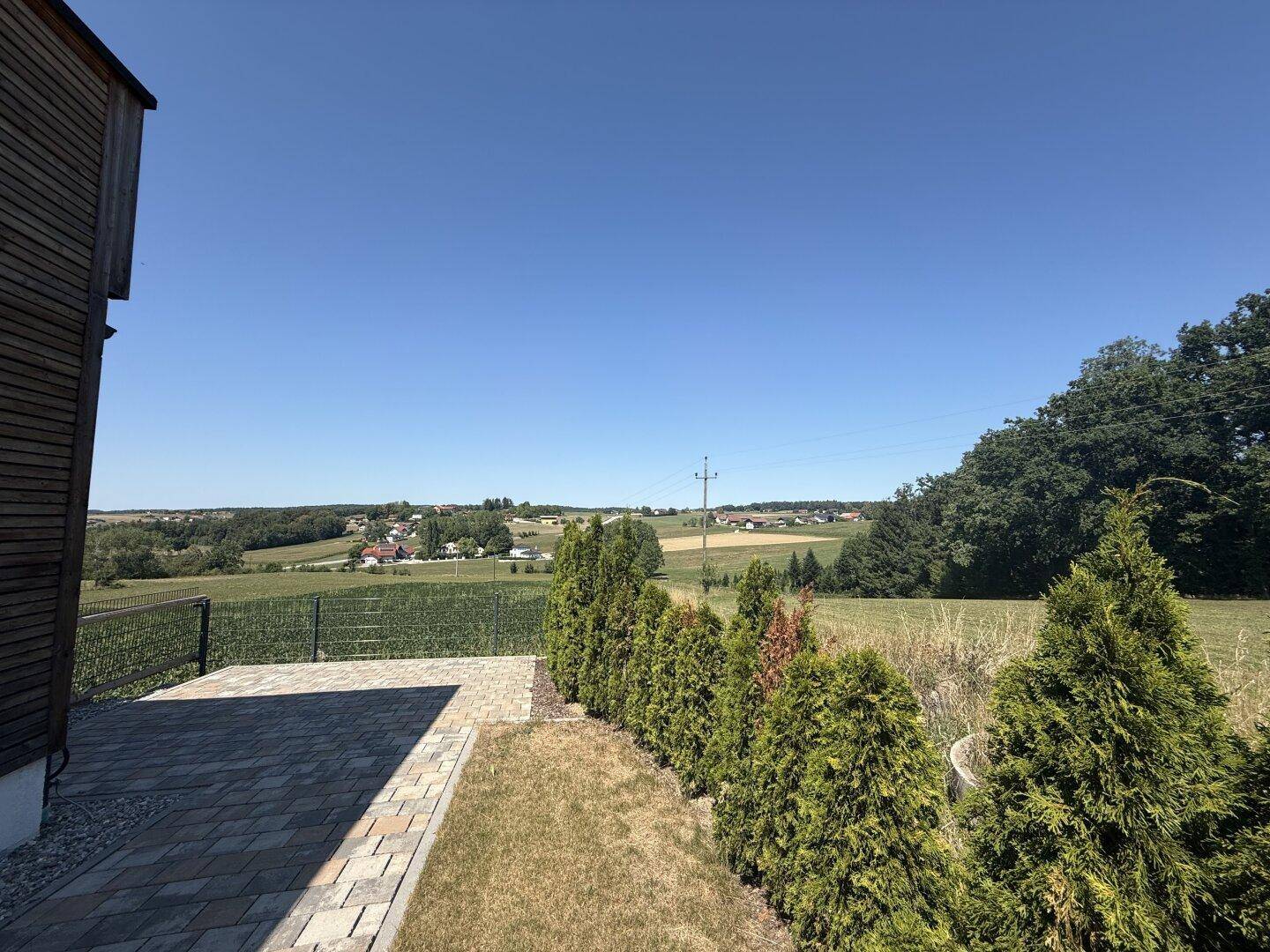 Seitlicher Blick auf das Haus mit gepflastertem Bereich und weitreichender Landschaftsaussicht.