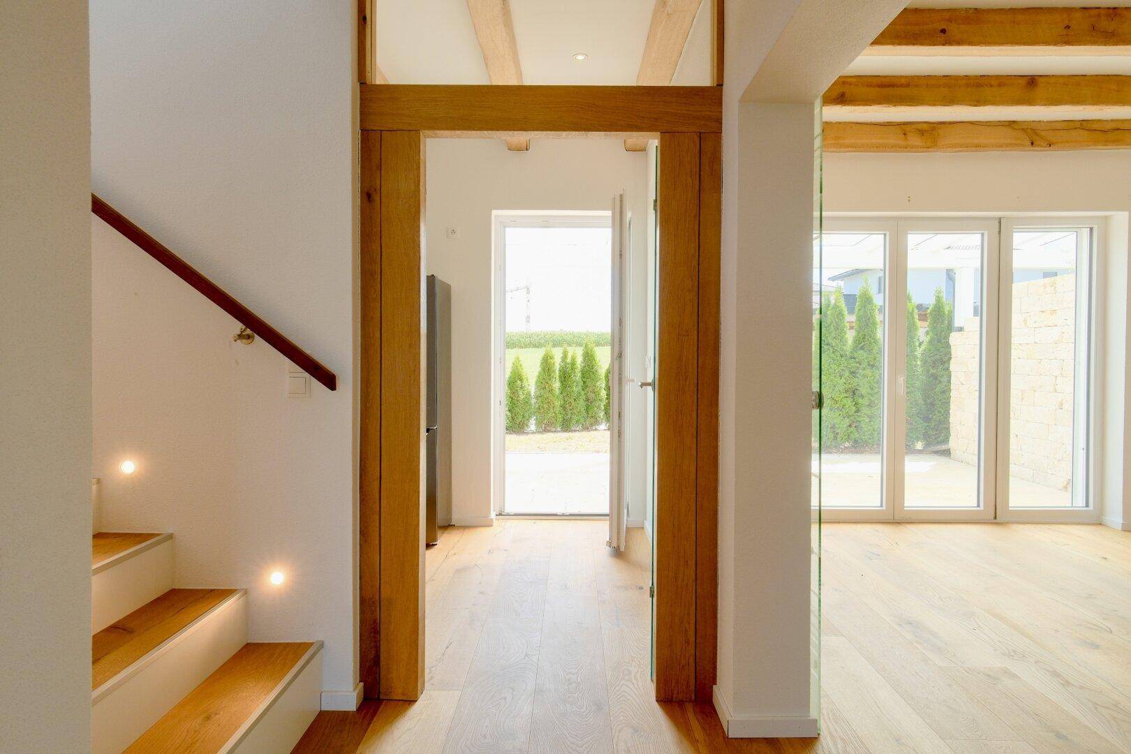 Eingangsbereich mit Holzbalken, Eichenparkett und Blick ins Grüne durch große Fenster.