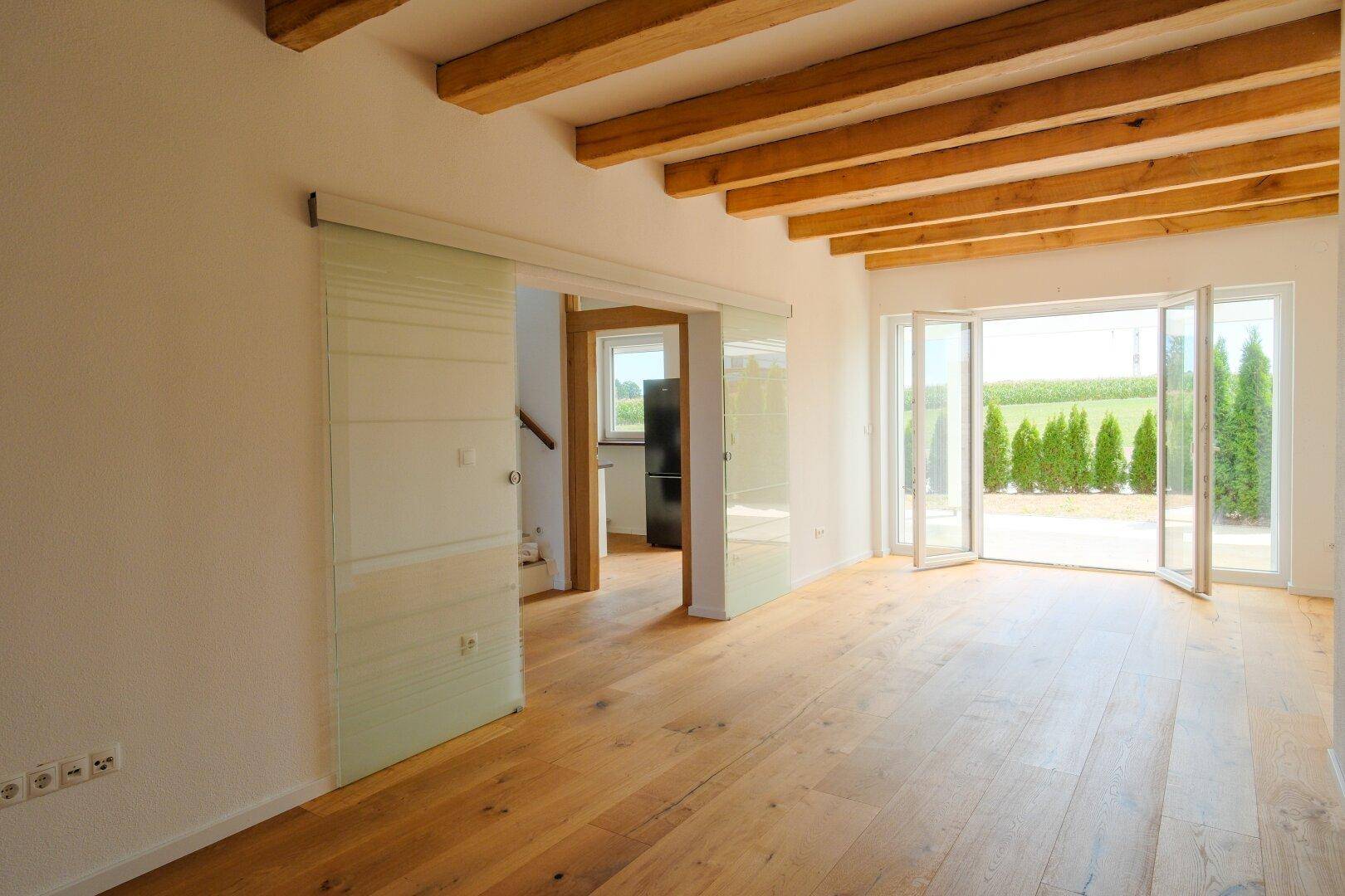 Geräumiges Wohnzimmer mit Holzbalkendecke, Eichenparkett und Zugang zur Terrasse.