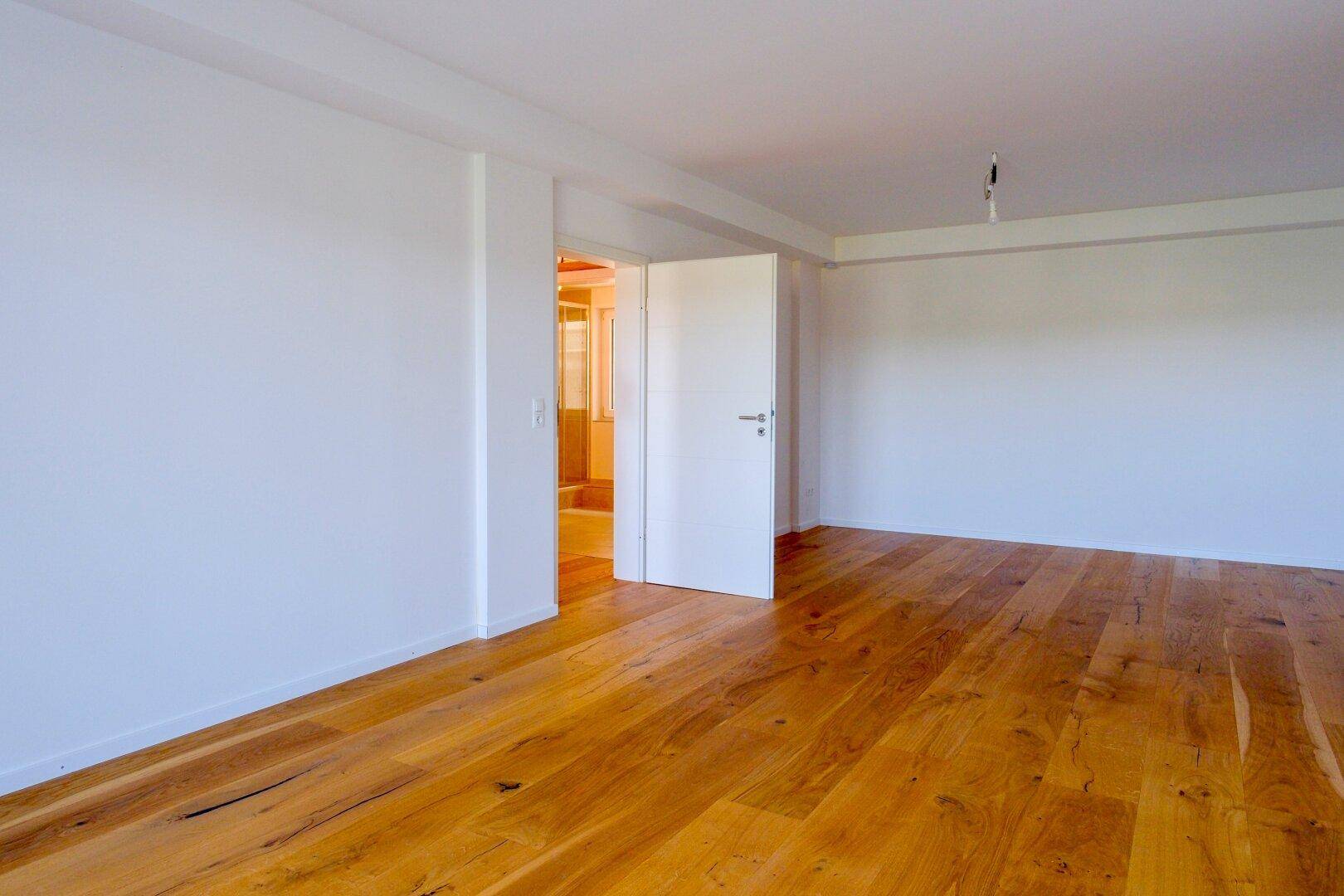 Geräumiges Zimmer mit hellem Eichenparkett und weiß gestrichenen Wänden.
