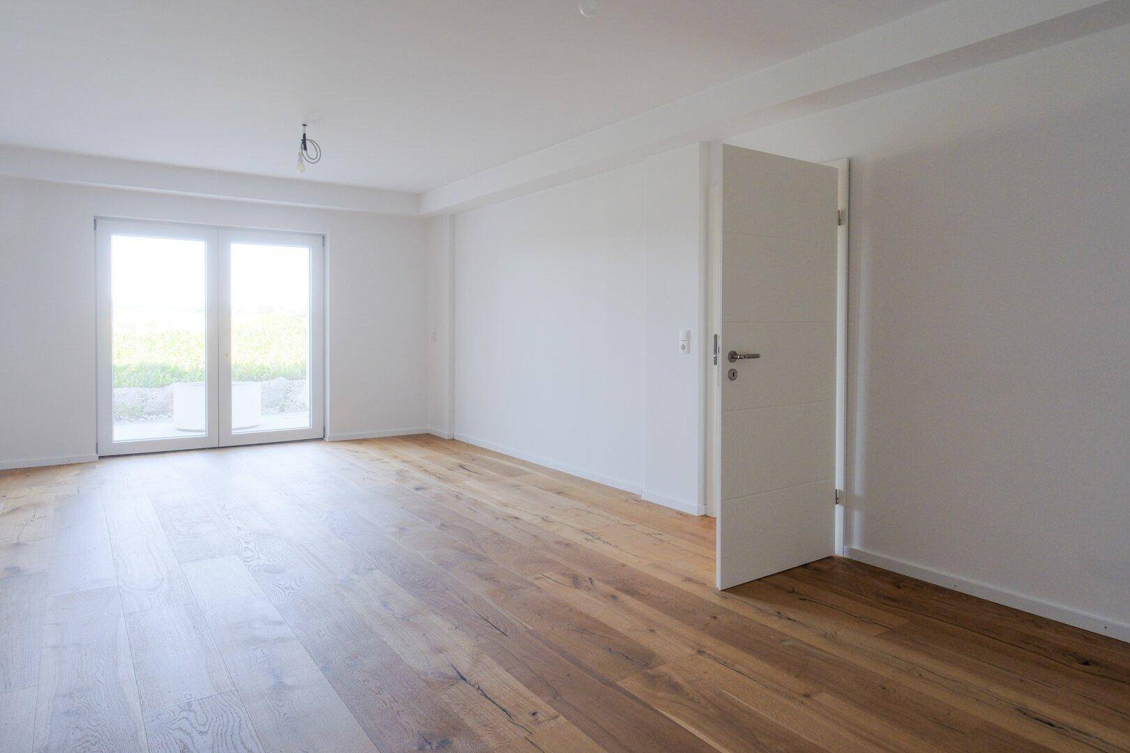 Helles Zimmer mit Eichenparkett und Zugang zu einem Außenbereich.