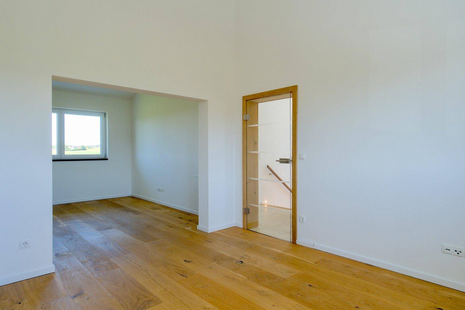 Heller Wohnbereich mit Eichenparkett, großem Fenster und Glastür.