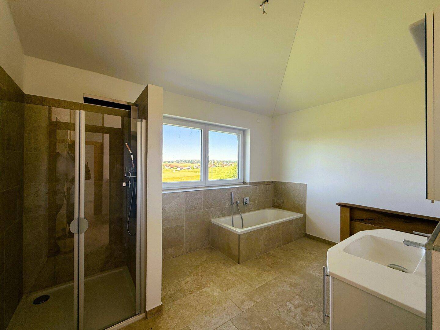 Geräumiges Badezimmer mit Dusche, Badewanne, Waschtisch und Fenster mit Aussicht.