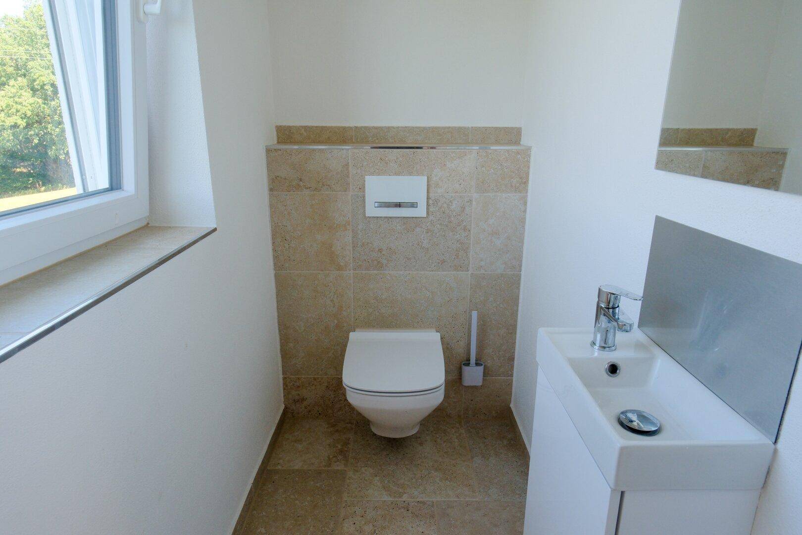 Modernes Gäste-WC mit Wand-WC, kleinem Waschbecken und Fenster.