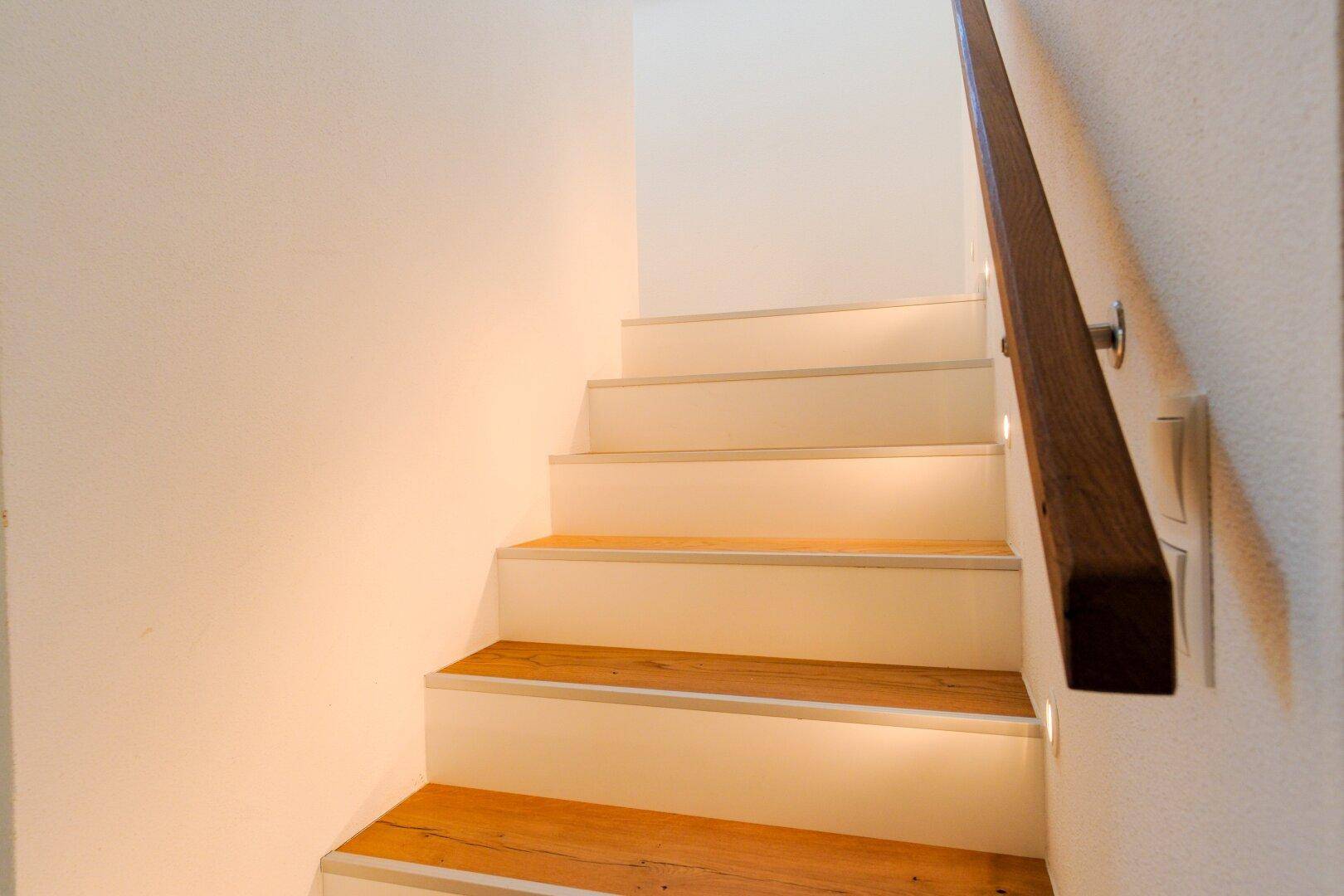 Elegante Holztreppe mit integrierter Beleuchtung und dunklem Holzhandlauf.