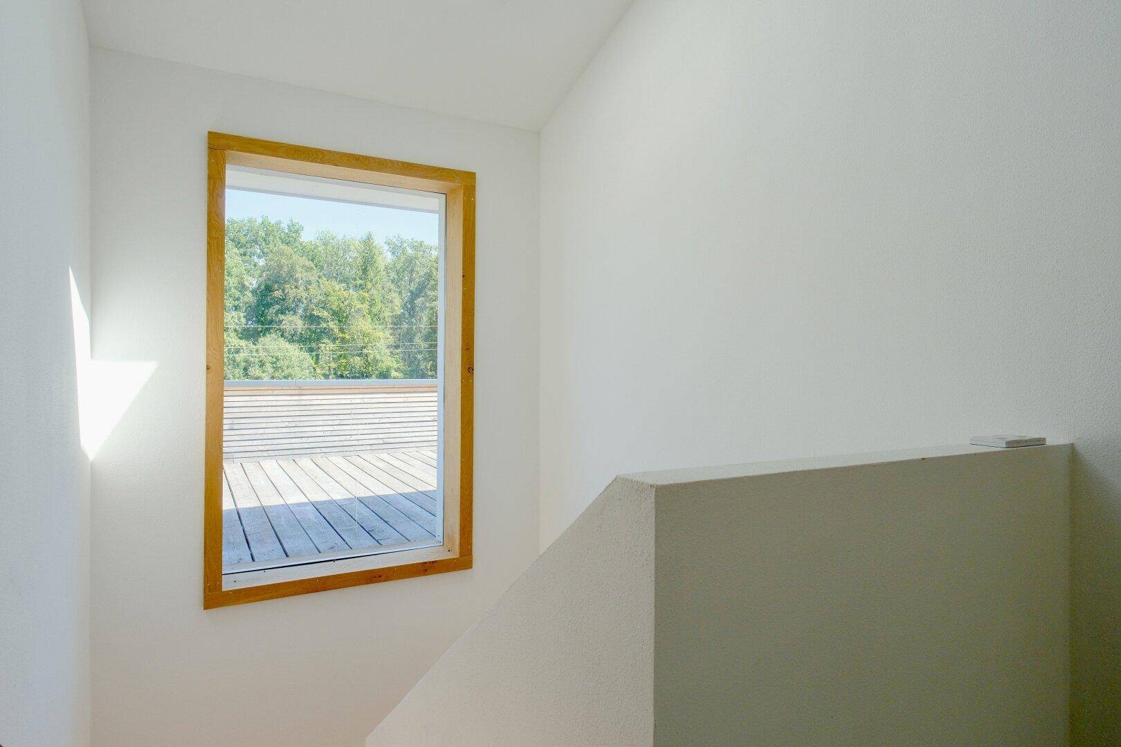 Helles Treppenhaus mit großem Fenster und Blick auf die Dachterrasse.