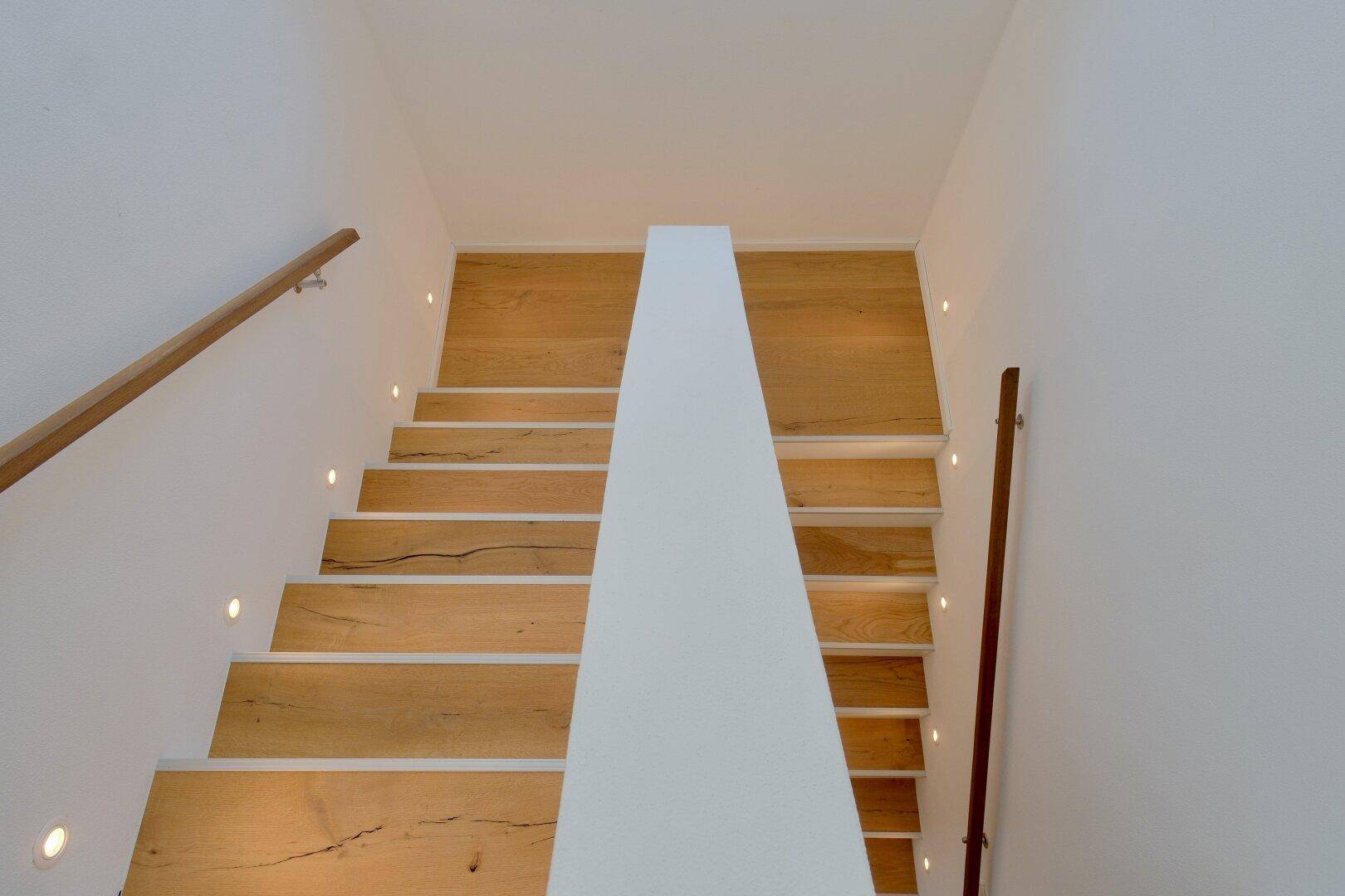 Moderne Holztreppe mit integrierter Stufenbeleuchtung und weißem Geländer.