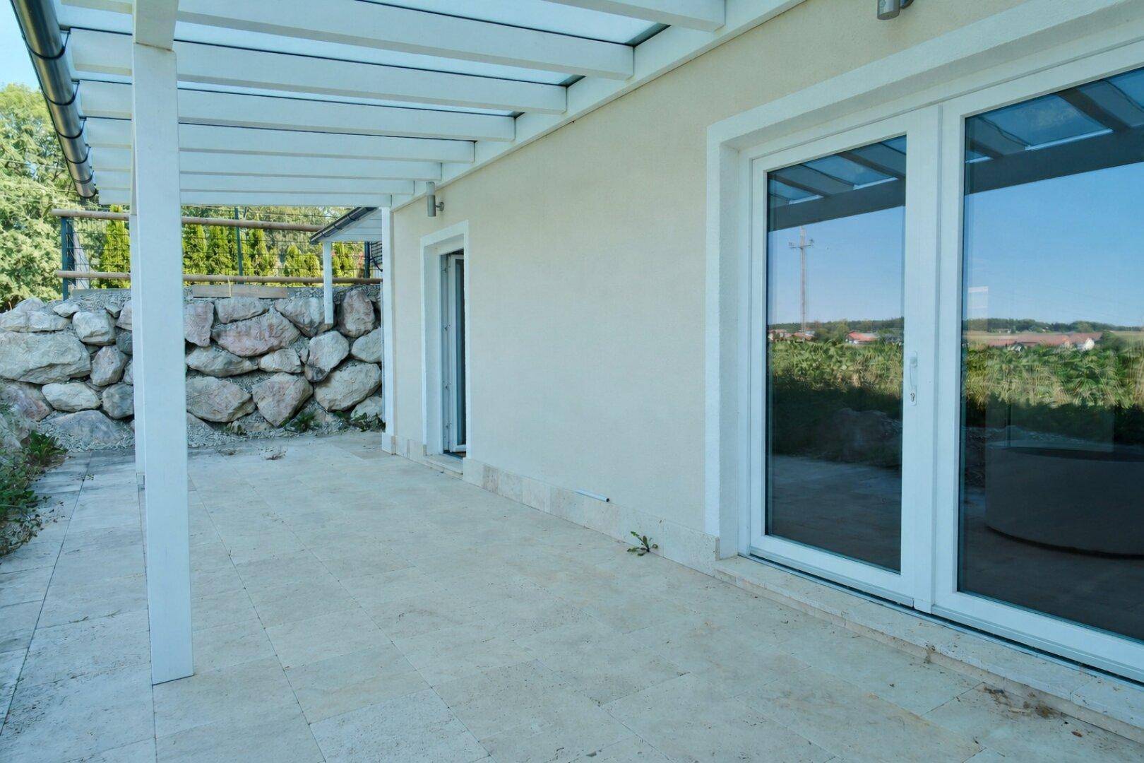 Helle Terrasse mit Steinboden und großen Fenstertüren zum Innenbereich.
