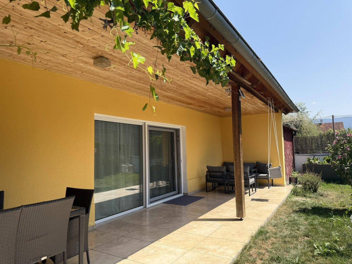 Überdachte Terrasse mit Gartenmöbeln und Zugang zum Haus durch große Glasschiebetüren.