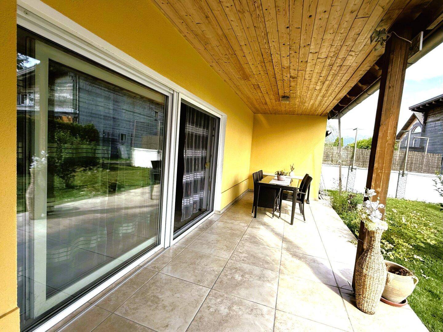 Überdachte Terrasse mit Fliesenboden und Sitzgelegenheiten, direkt am Haus gelegen.