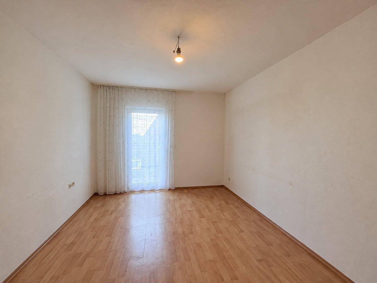 Leeres Zimmer mit Laminatboden und Zugang zu einem Balkon oder einer Terrasse.