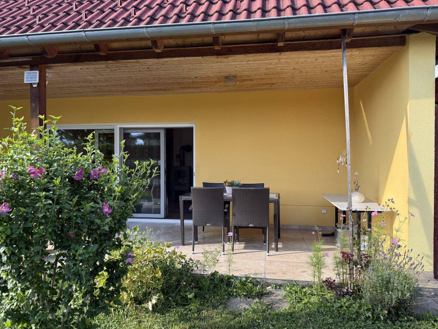 Gemütliche überdachte Terrasse mit Gartenmöbeln und blühenden Pflanzen im Außenbereich.