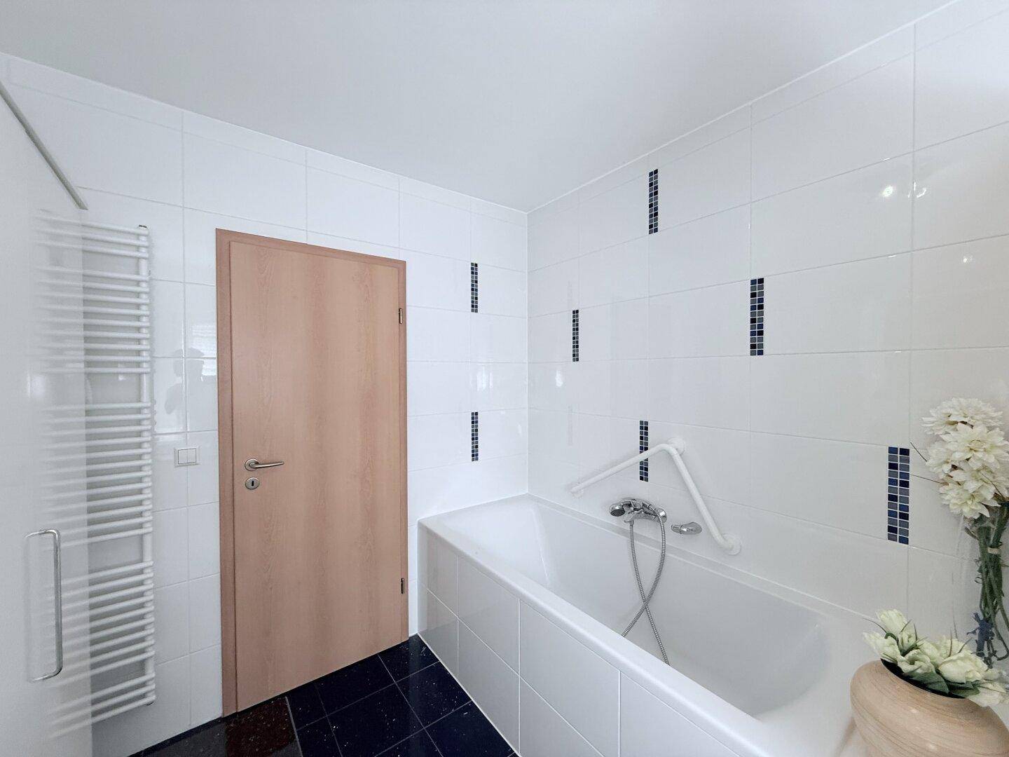 Modernes Badezimmer mit Badewanne, weißen Fliesen und beheiztem Handtuchhalter.