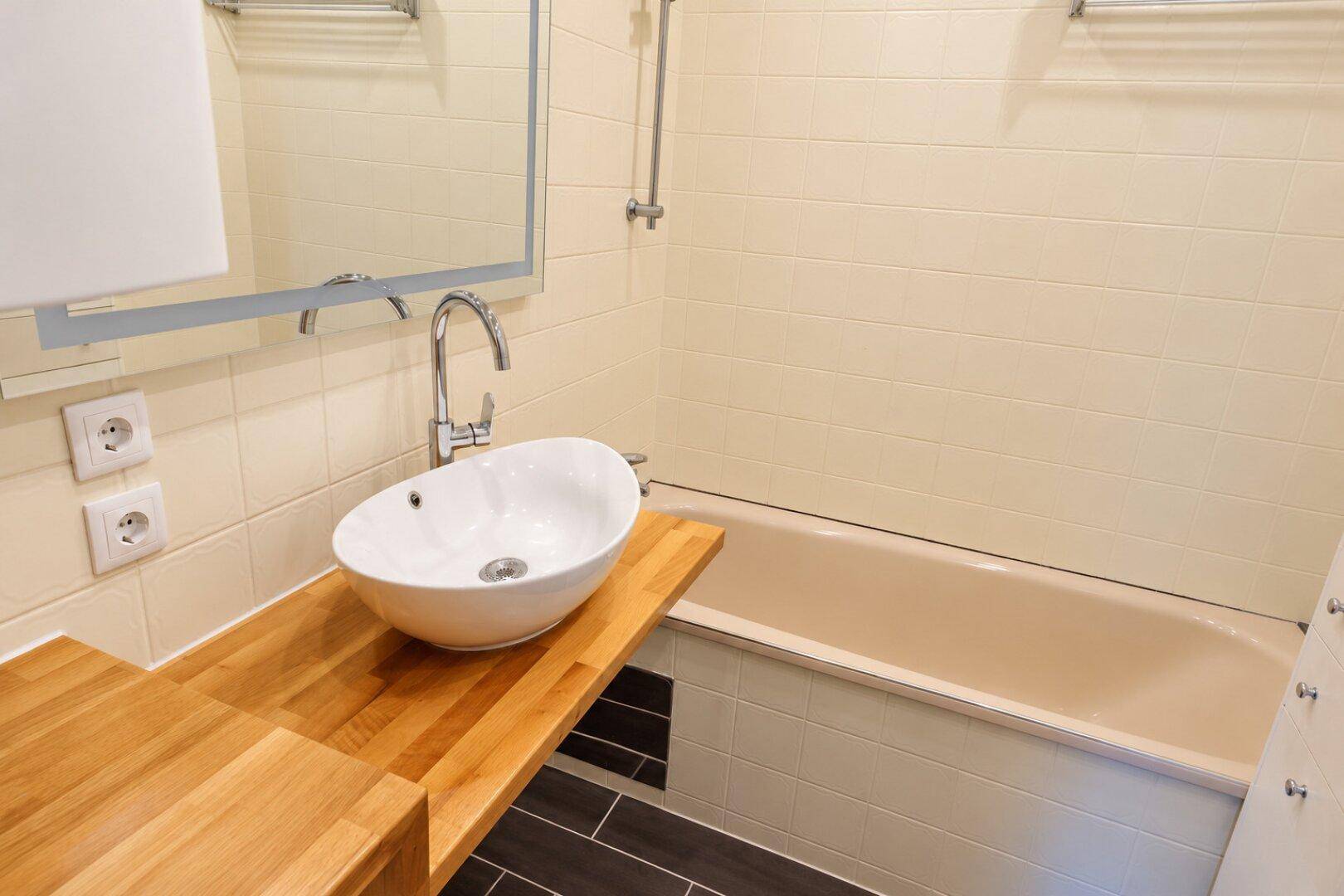 Helles Badezimmer mit modernem Aufsatzwaschbecken, Holzplatte und Badewanne.