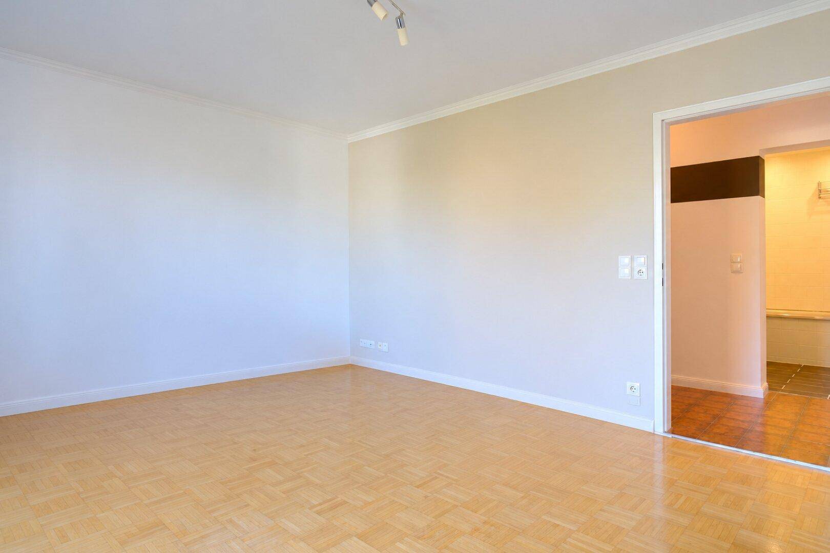 Geräumiges Zimmer mit Parkettboden und offenem Durchgang zu einem angrenzenden Bereich.