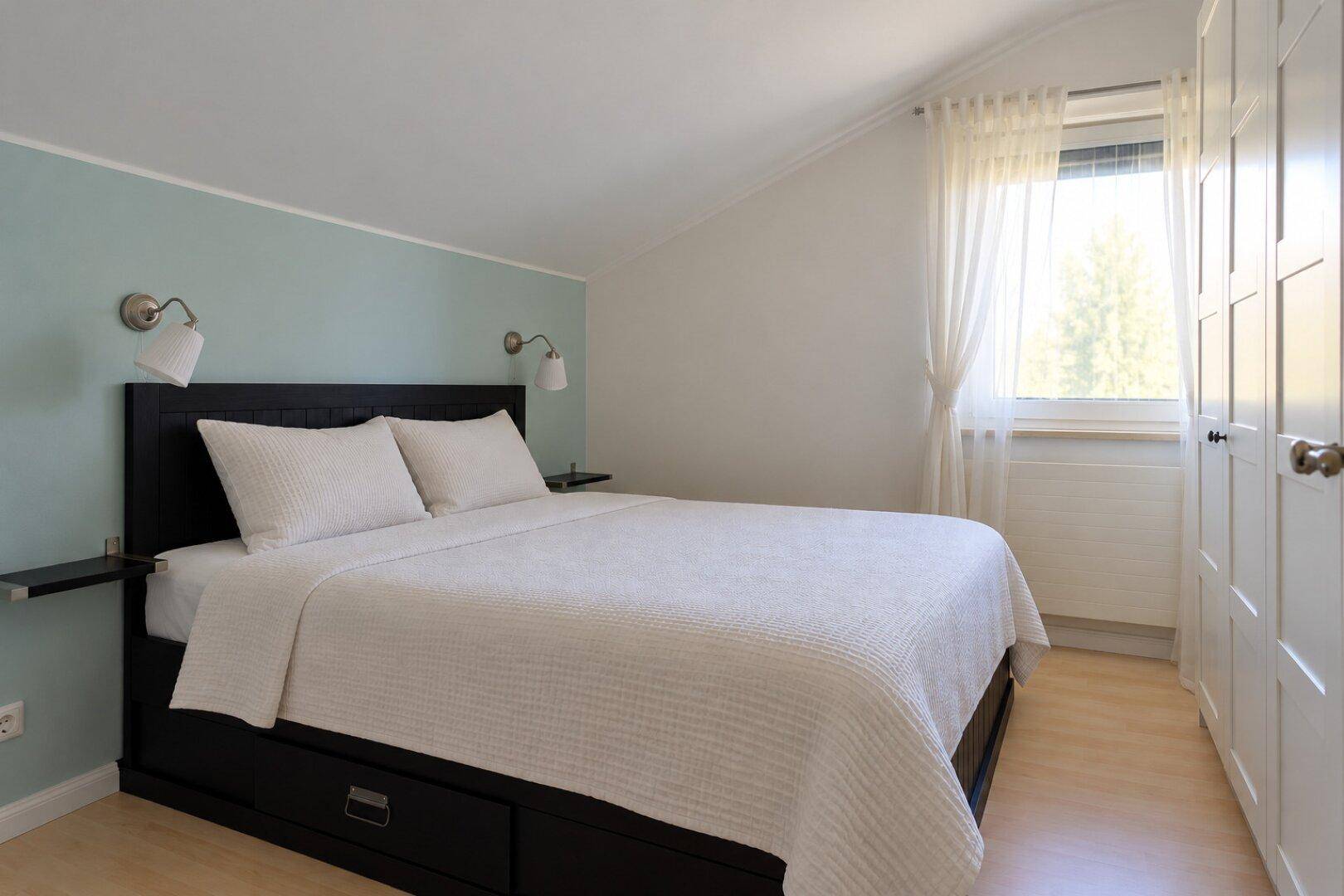 Gemütliches Schlafzimmer mit Doppelbett, hellblauer Akzentwand und Dachschräge.