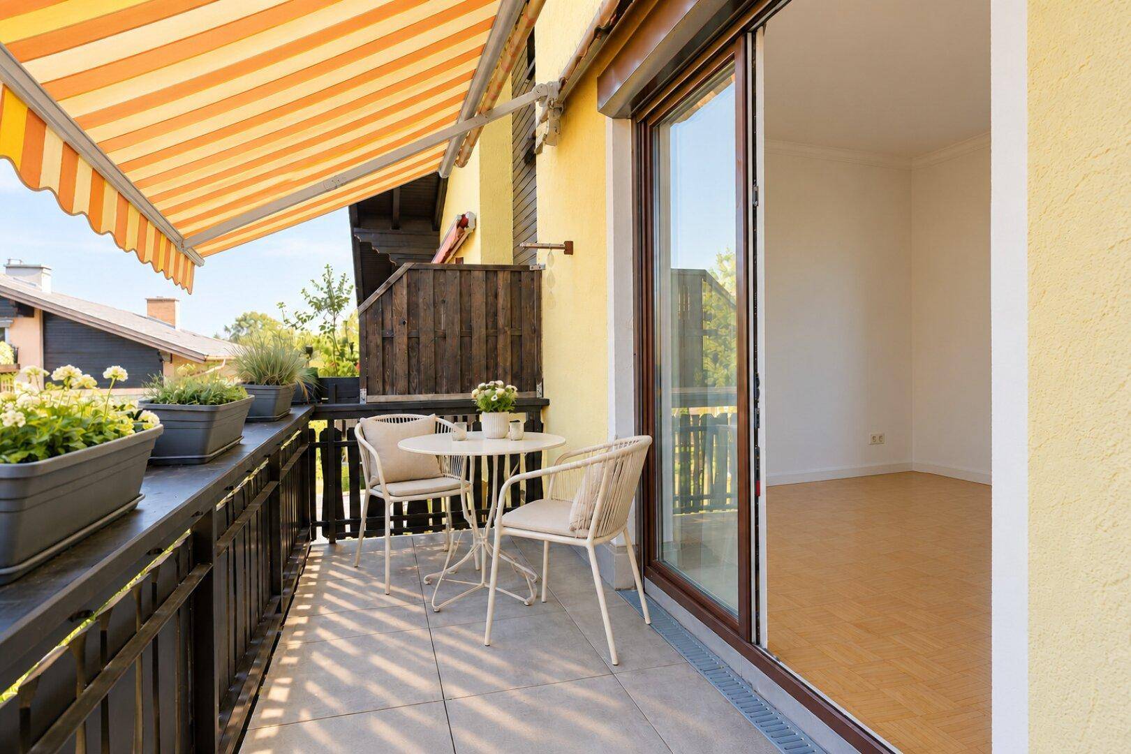 Heller Balkon mit Fliesenboden, kleiner Sitzgruppe und direktem Zugang zu einem Innenraum.