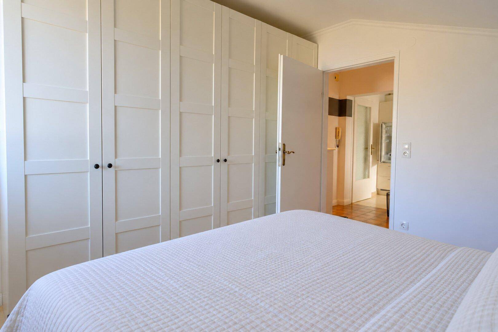 Schlafzimmer mit einer Reihe von weißen Einbauschränken und Zugang zu einem weiteren Raum.