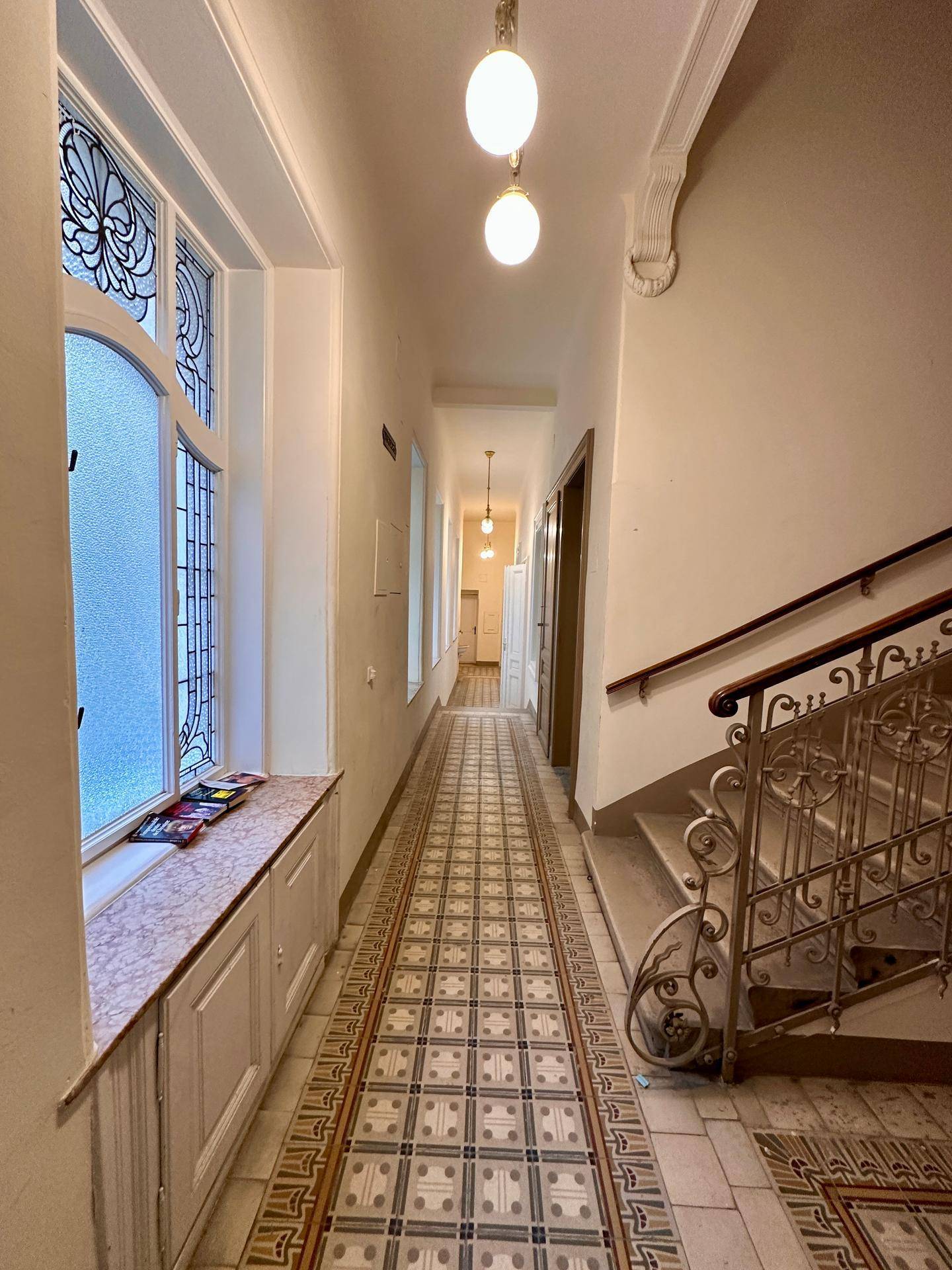 Heller Flur mit großen Fenstern, gemusterten Fliesen und einer eleganten Treppe im Altbau.