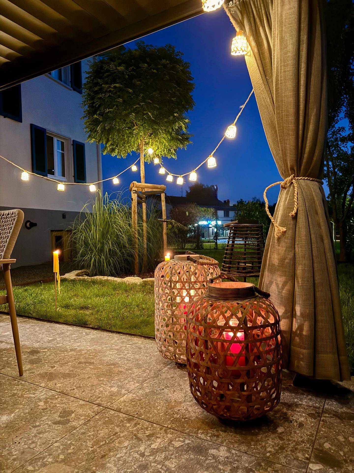 Gemütliche Abendbeleuchtung auf der Terrasse mit Lichterketten und dekorativen Laternen.