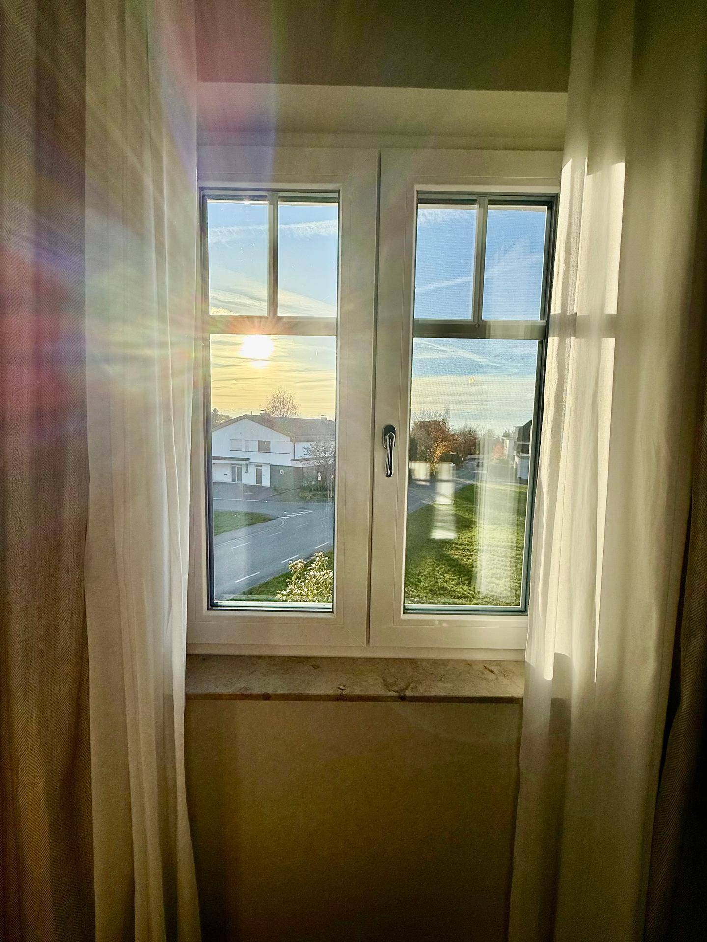 Fensterblick auf eine Wohnsiedlung bei Sonnenuntergang, mit hellem Himmel.