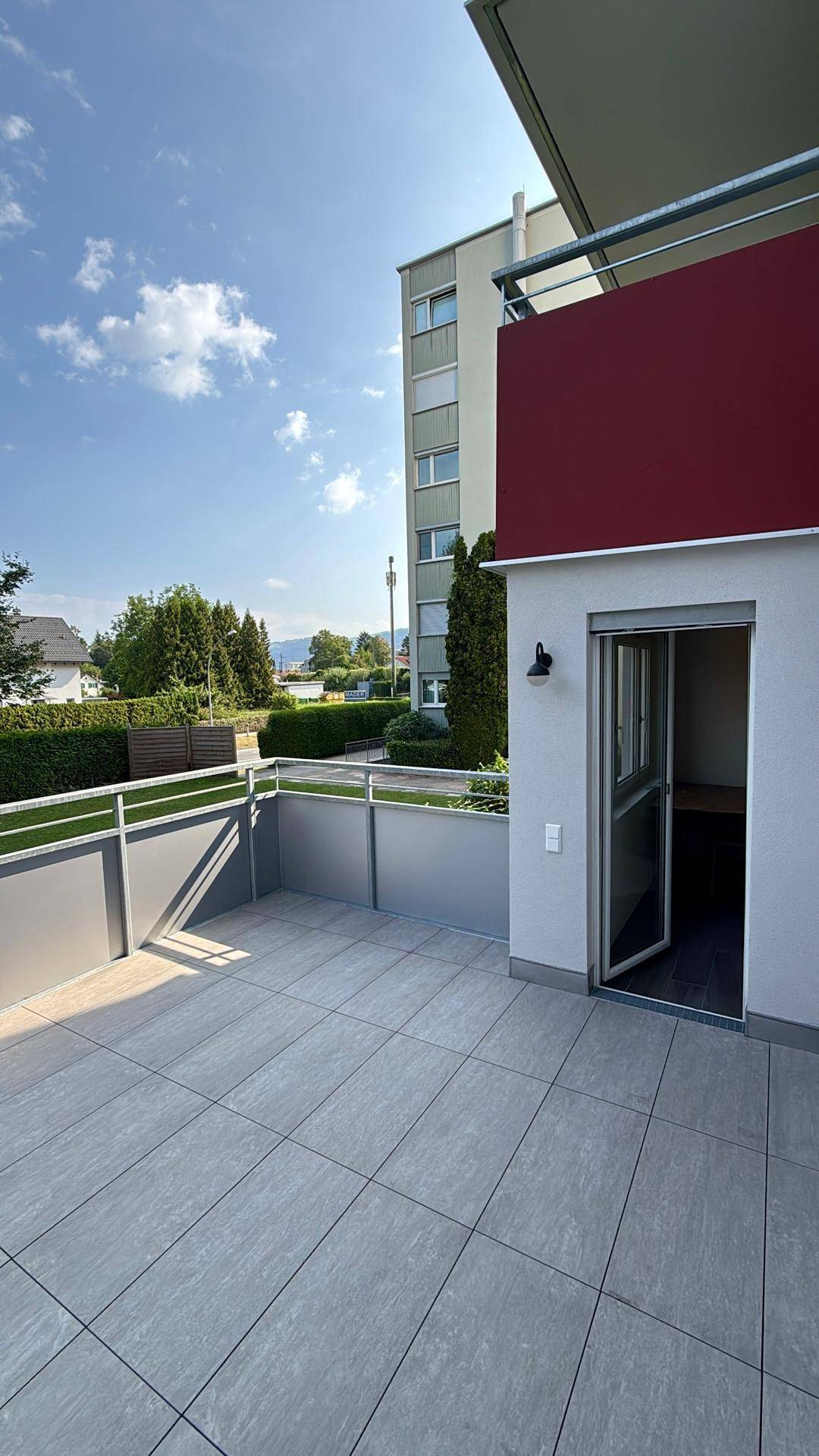 Große geflieste Terrasse mit Blick ins Grüne und angrenzendem Gebäude.