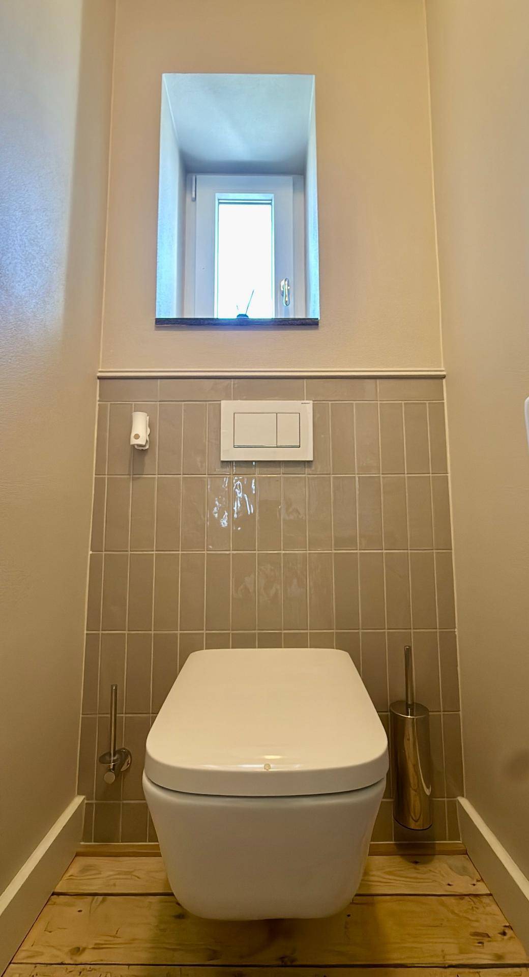 Nahaufnahme der wandhängenden Toilette mit Fliesenwand und Fenster im Gäste-WC.