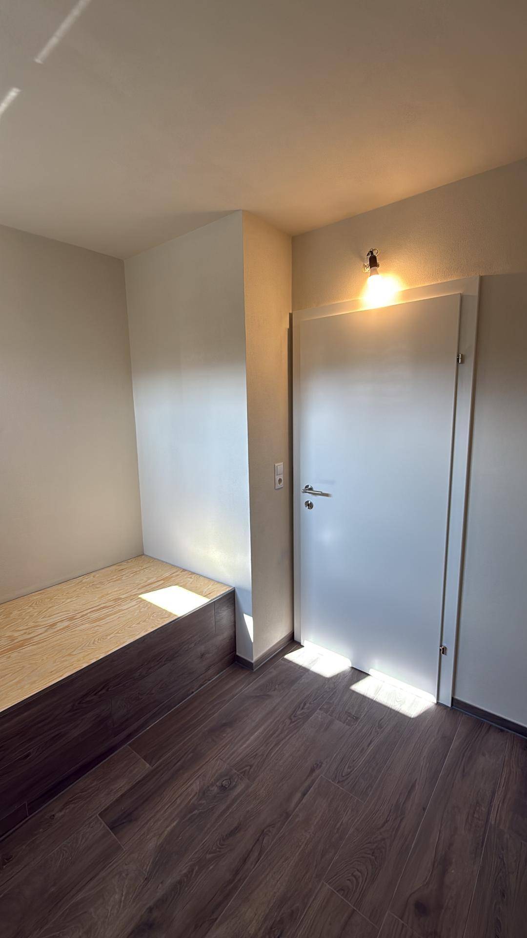 Zimmer mit Holzboden und einer erhöhten Holzplattform, ideal als Schlafbereich.