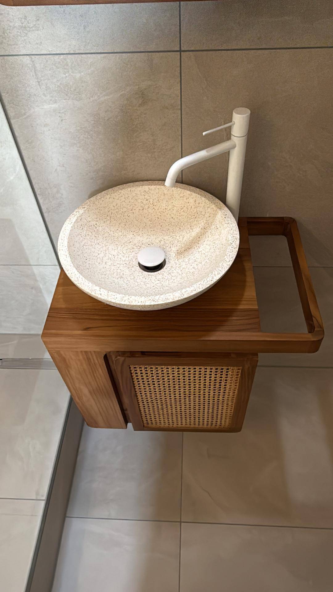 Modernes Waschbecken auf Holzunterschrank mit Rattan-Details und weißem Wasserhahn.