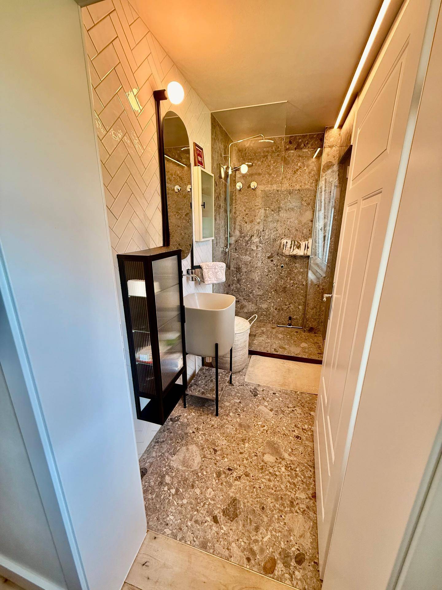 Modernes Badezimmer mit begehbarer Dusche, Steinboden und weißen Wandfliesen.