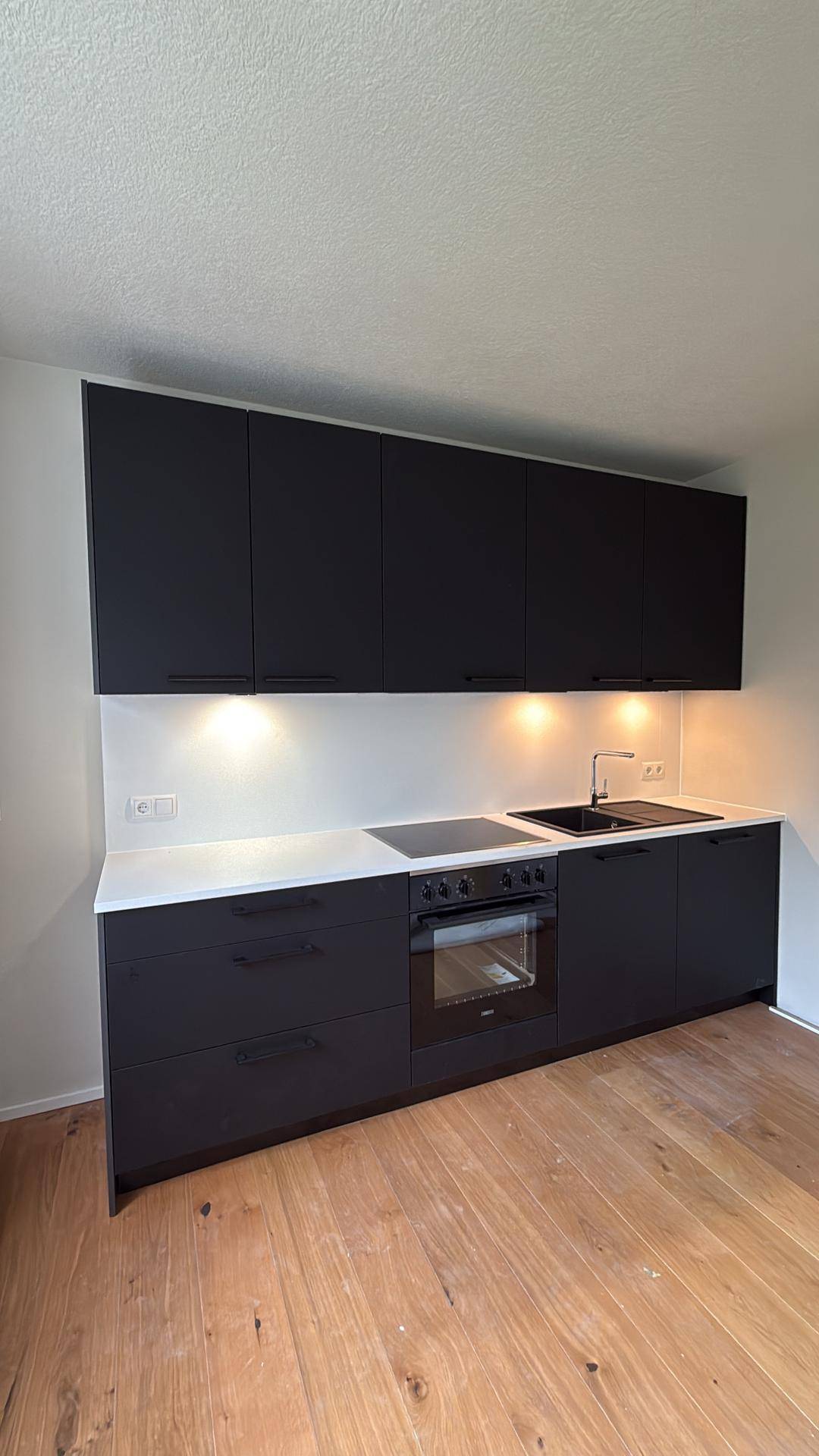 Moderne Einbauküche mit schwarzen Schränken, heller Arbeitsplatte und Holzboden.