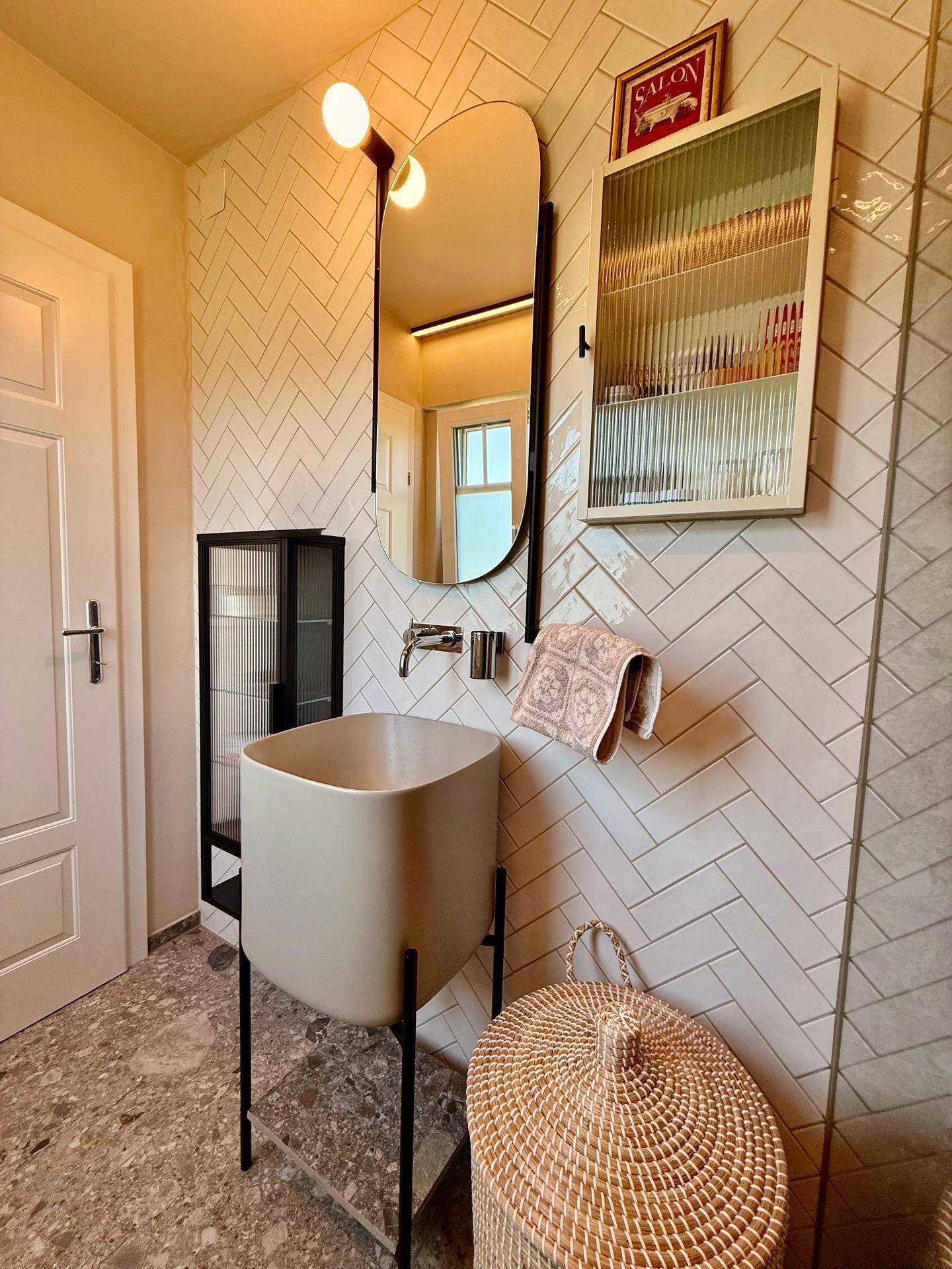 Badezimmer mit stilvollem Waschbecken, großem Spiegel und weißen Wandfliesen im Fischgrätmuster.