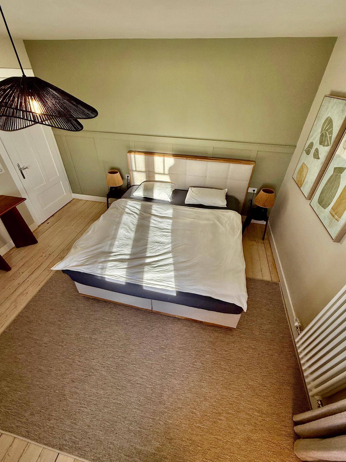 Schlafzimmer mit großem Bett, grüner Akzentwand und Teppichboden.