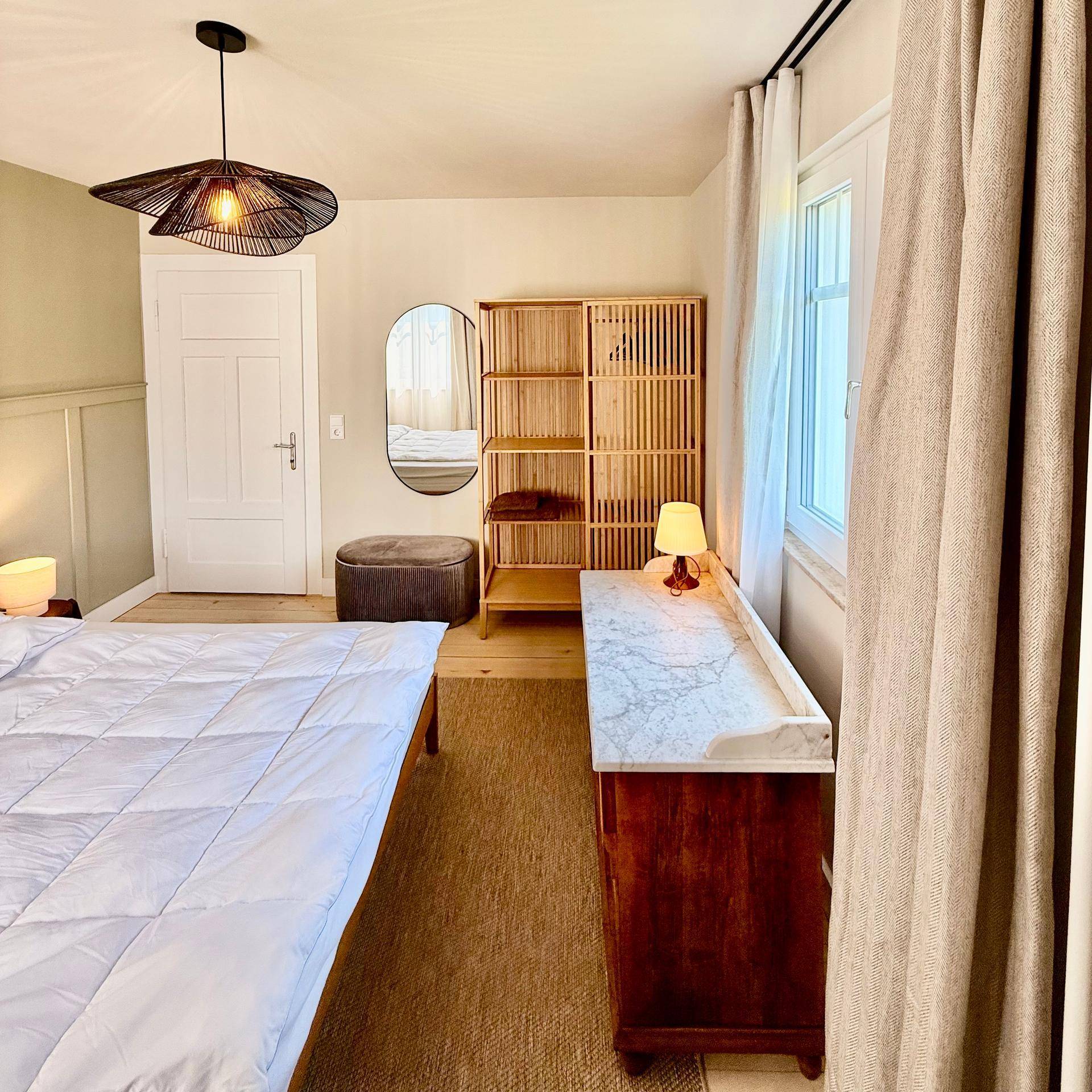 Schlafzimmer mit Bett, Kommode mit Marmorplatte und offenem Holzregal.