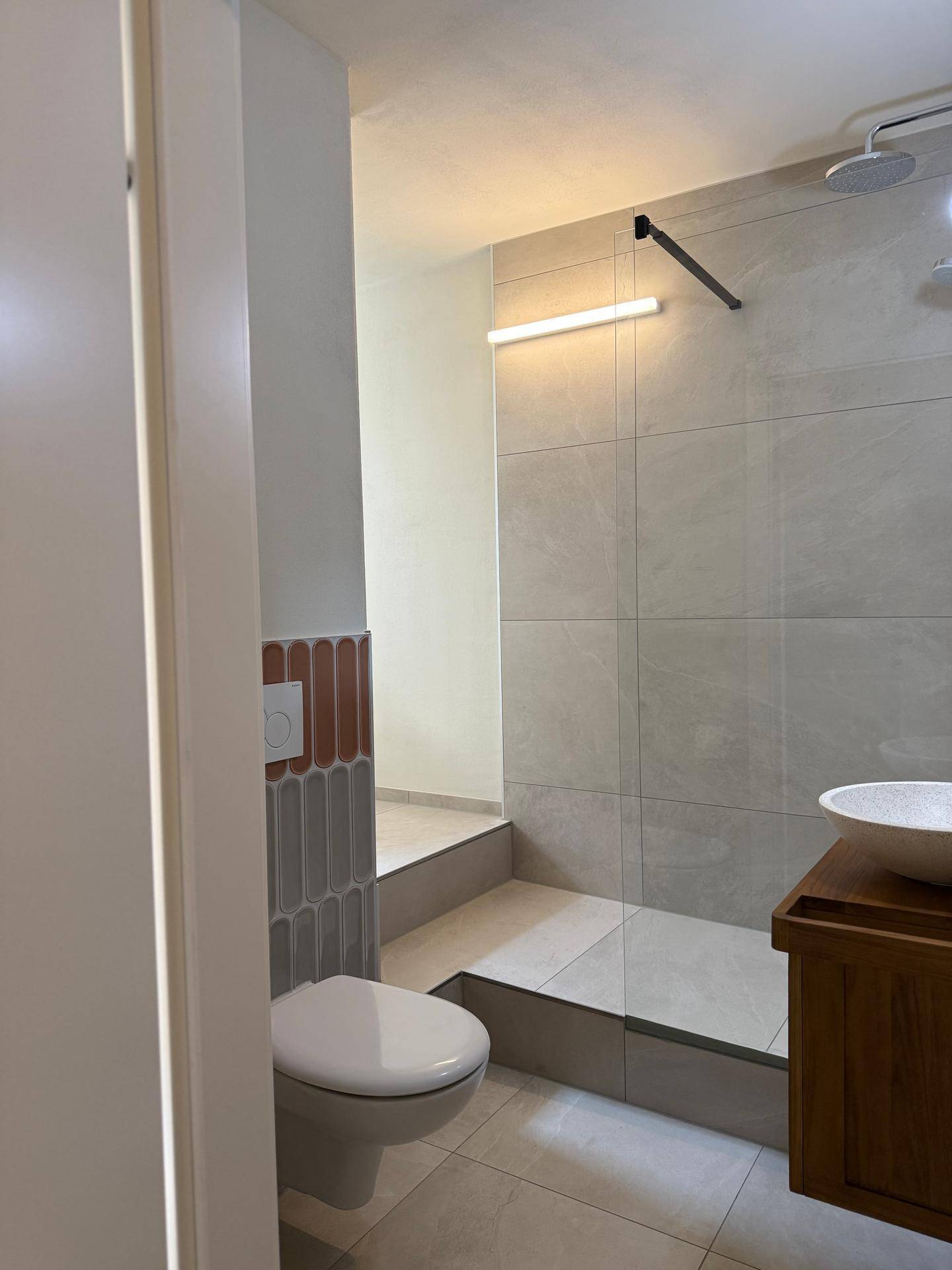 Helles Badezimmer mit Toilette und moderner Dusche, teilweise gefliest.