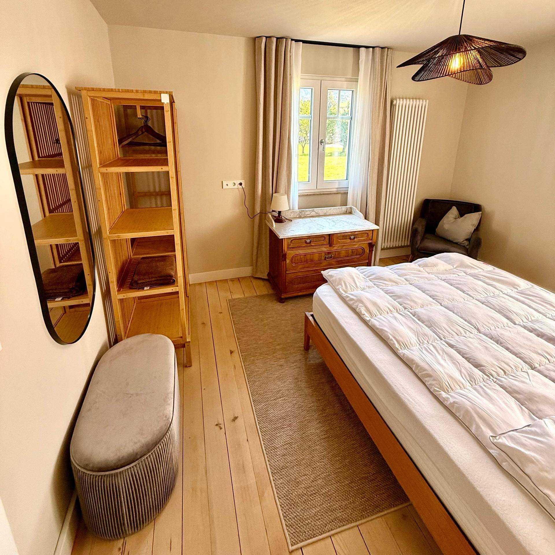 Schlafzimmer mit Bett, offenem Regal, Spiegel und einer antiken Kommode.