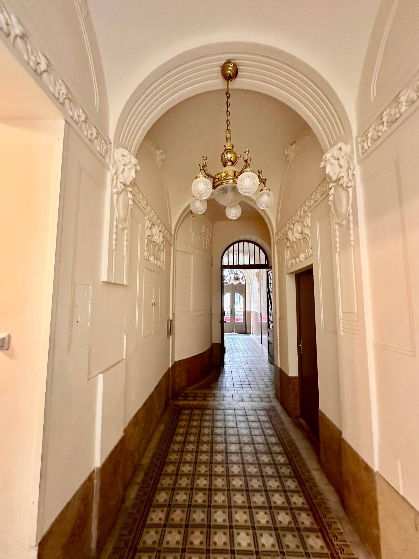 Langer Flur in einem Altbau mit gewölbter Decke, Stuckverzierungen und gemusterten Fliesen.