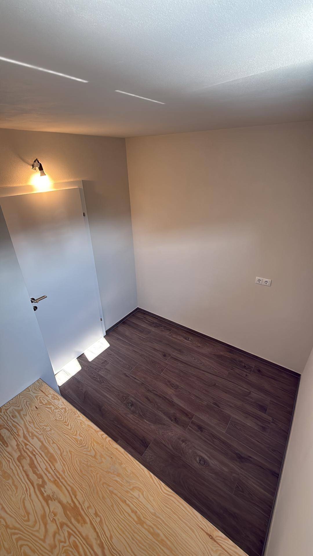 Geräumiges Zimmer mit dunklem Holzboden und einer hellen Holzplattform.