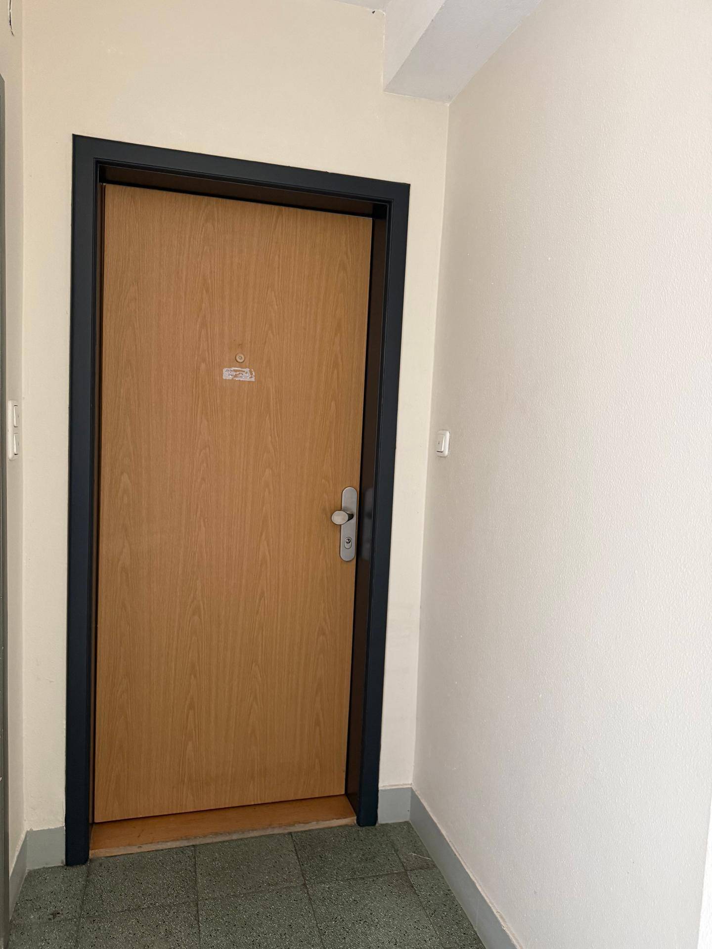 Eingangstür aus Holz mit dunklem Rahmen und gefliestem Boden im Flurbereich.