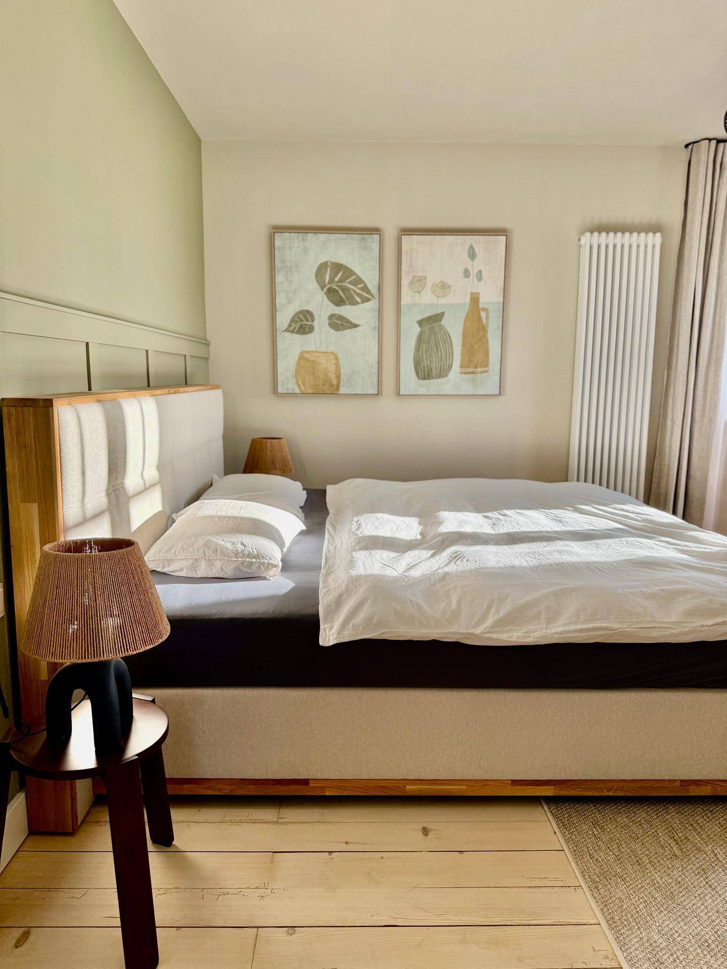 Detailansicht des Bettes im Schlafzimmer mit Kunstwerken und Nachttischlampe.