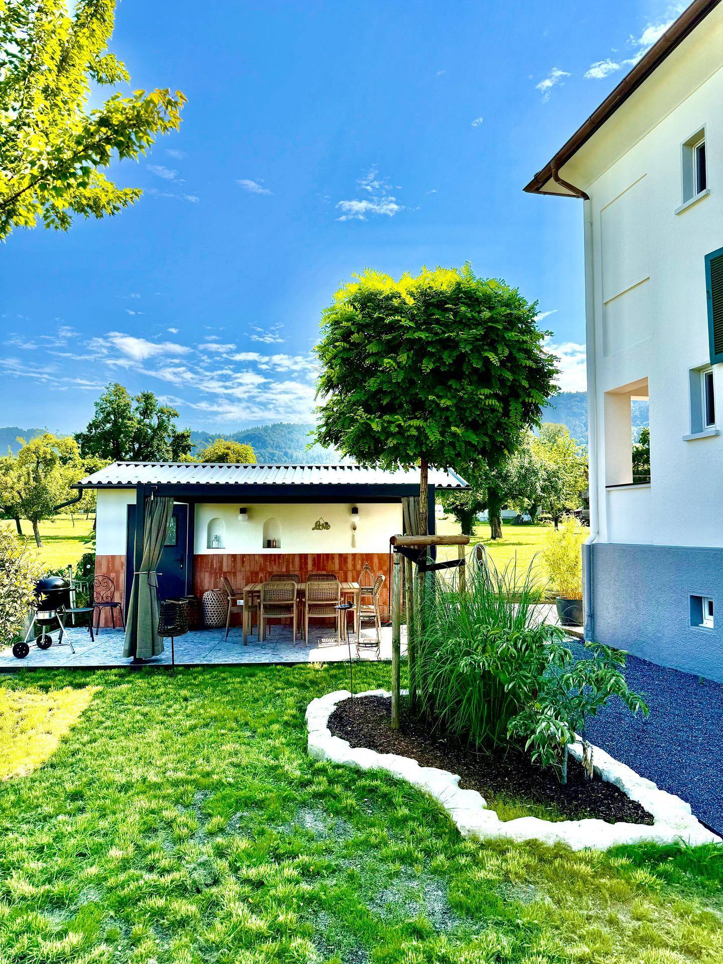 Gepflegter Gartenbereich mit Rasenfläche, Zierbaum und Blick auf das Haupthaus und die Terrasse.