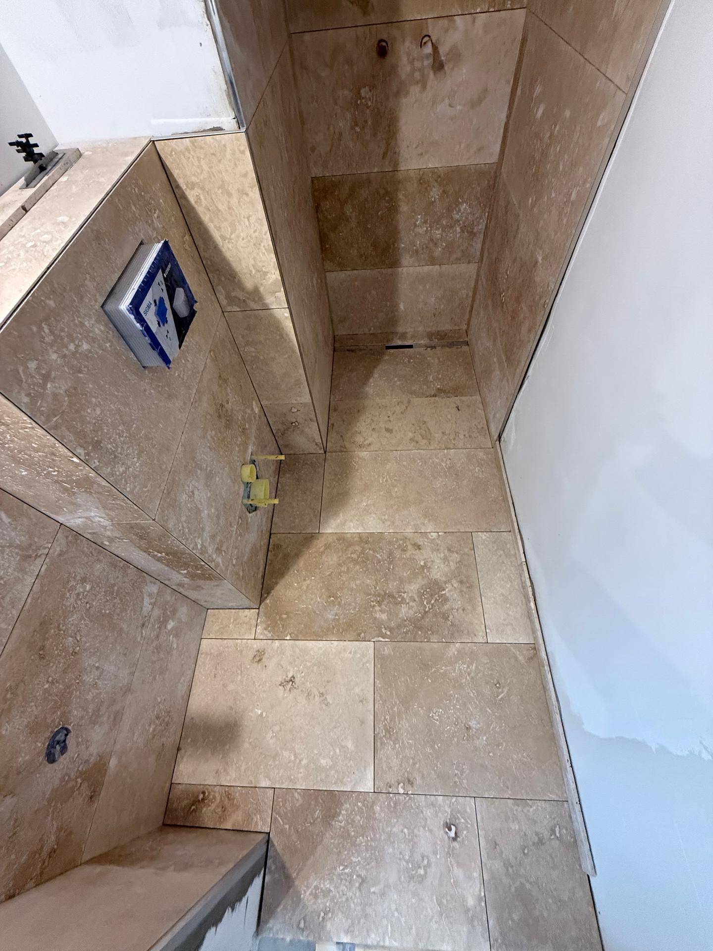 Detaillierte Ansicht des Badezimmers im Bau mit beigefarbenen Natursteinfliesen an Boden und Wänden.