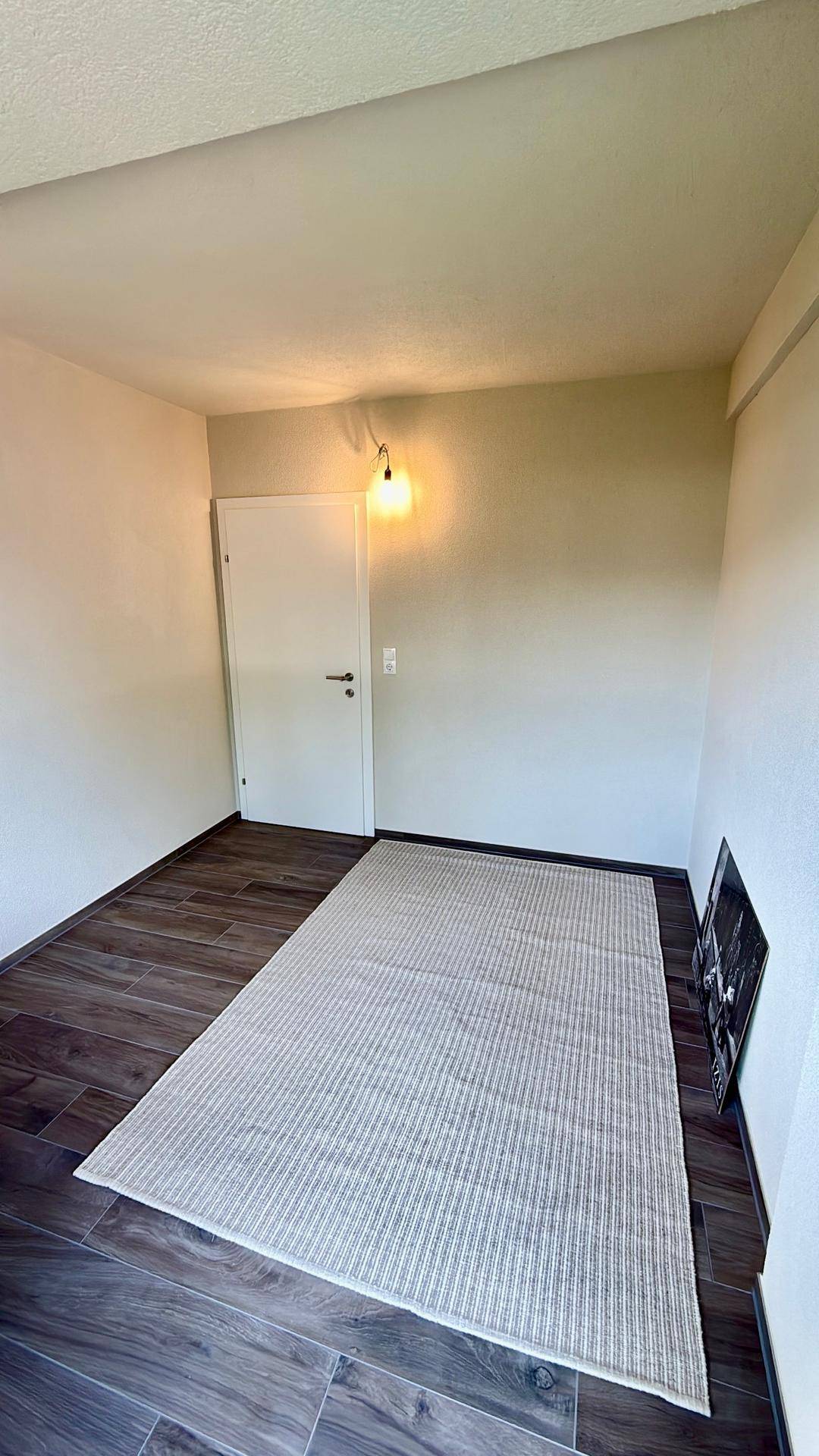 Leerer Raum mit Holzboden und einem Teppich, bereit zur individuellen Gestaltung.